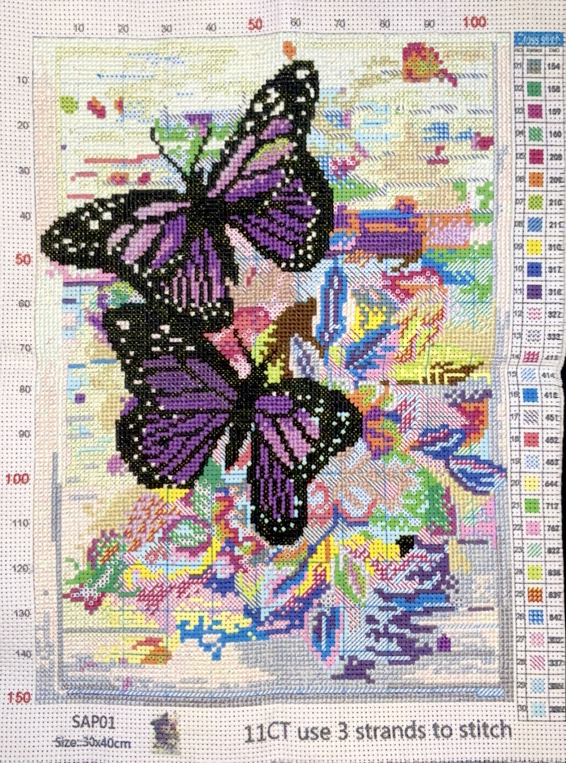 the frontside of a stamped cross stitch pattern with two purple butterflies surrounded by unstitched flowers