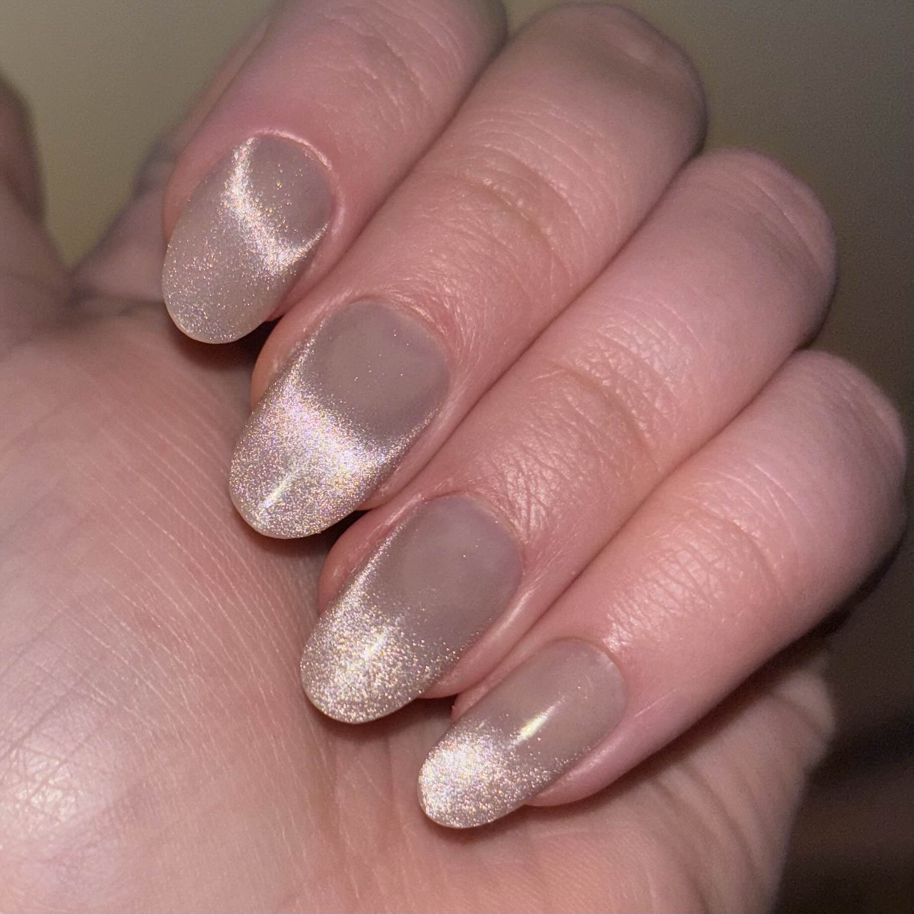 Beige, mid-length almond-shaped press-on nails. There's a sparkly streak on each nail simulating a cat eye effect.